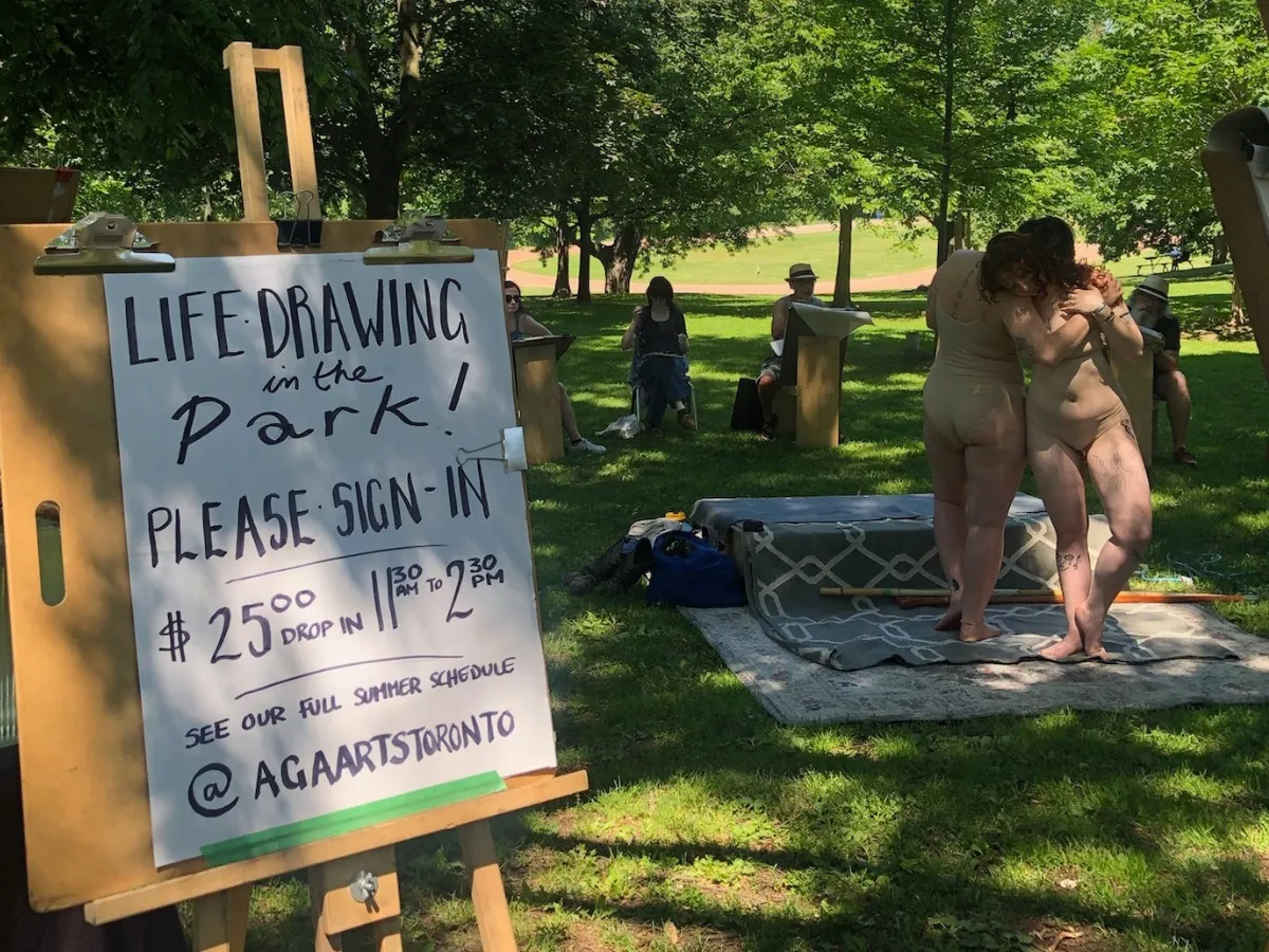 An easel sign reads "Life drawing in the park, please sign in, $25 drop-in, 11:30 to 2:30, @agaartstoronto" while two costumed models pose on a rug and artists draw.