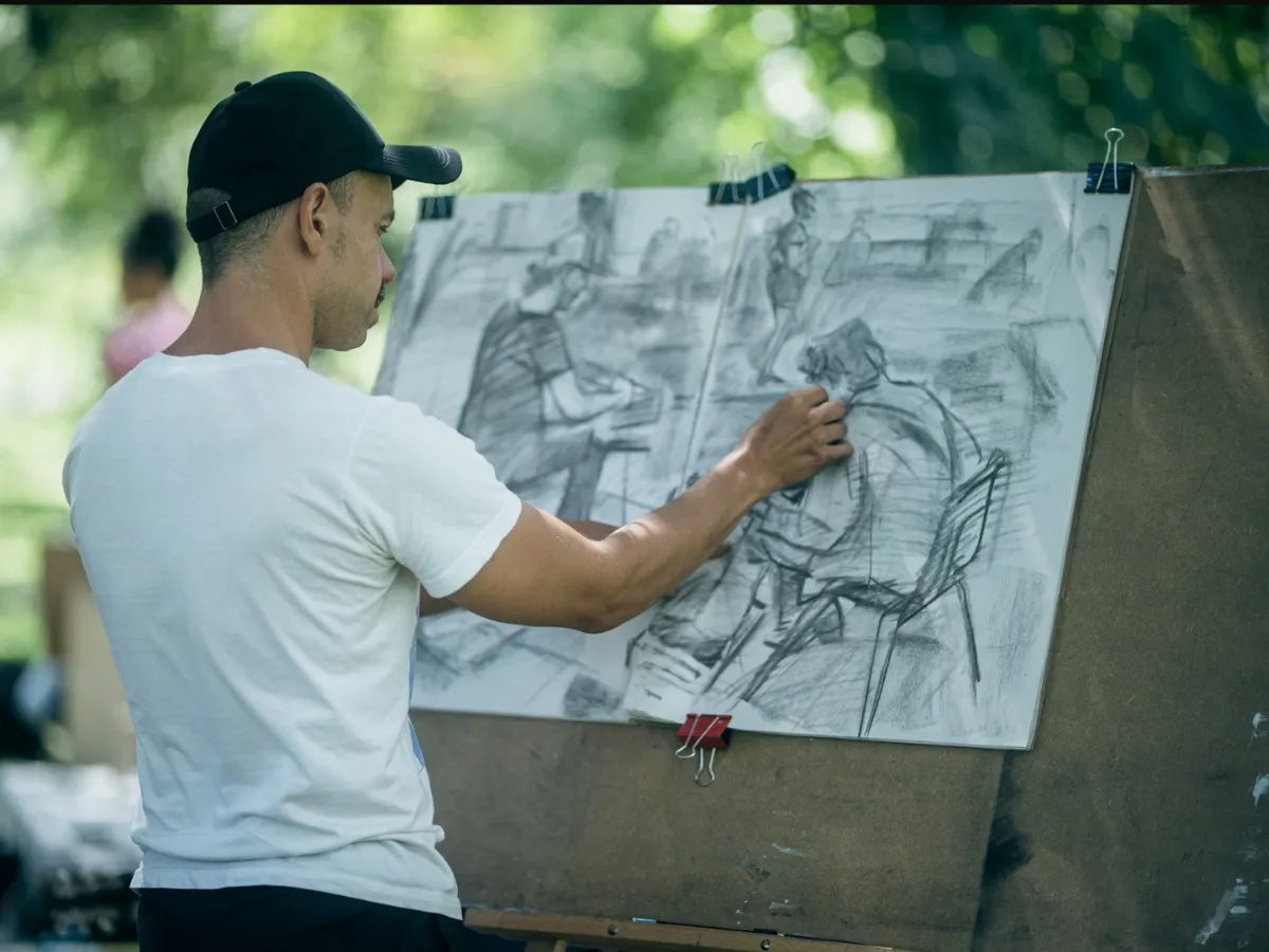 An artist in a cap works on a large charcoal drawing of the musicians.