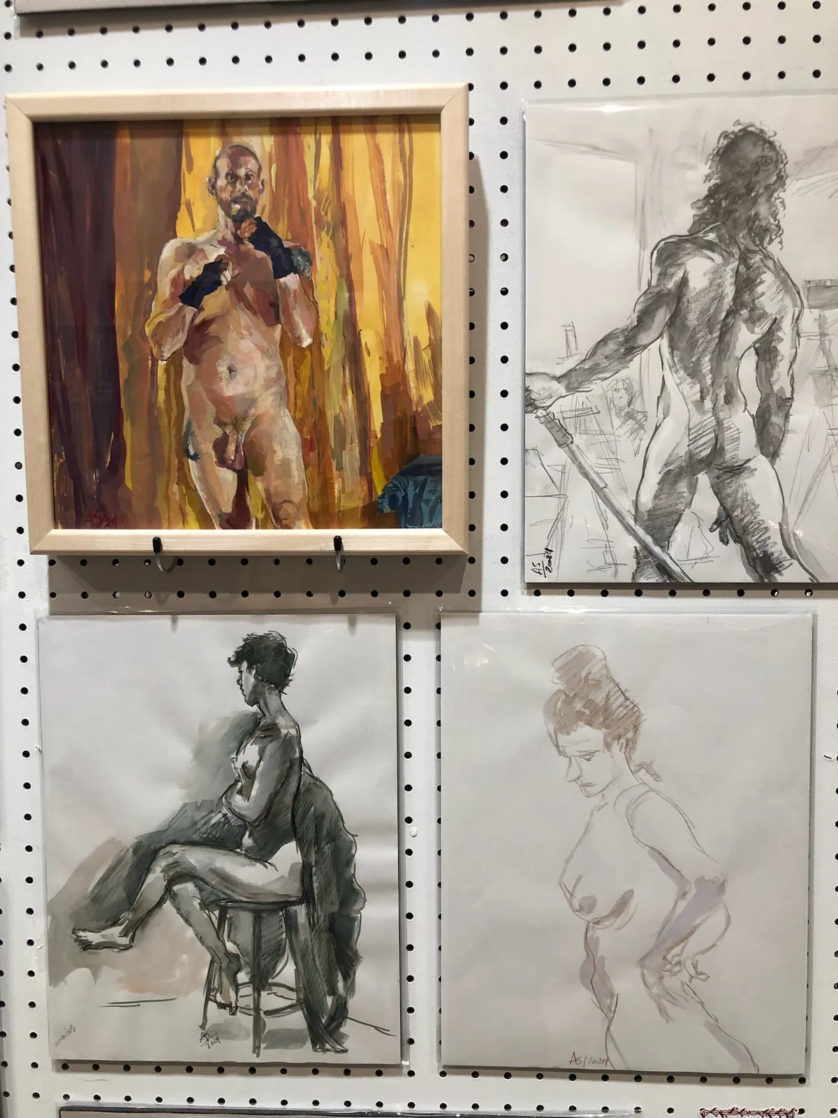 Four figure studies on a pegboard wall: an oil painting of a standing nude man and three drawings.