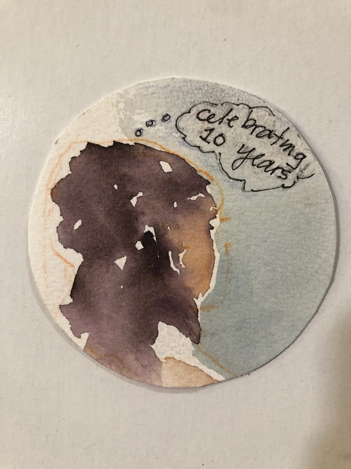 A small round watercolour of a figure seen from behind, with a thought bubble reading "celebrating 10 years".