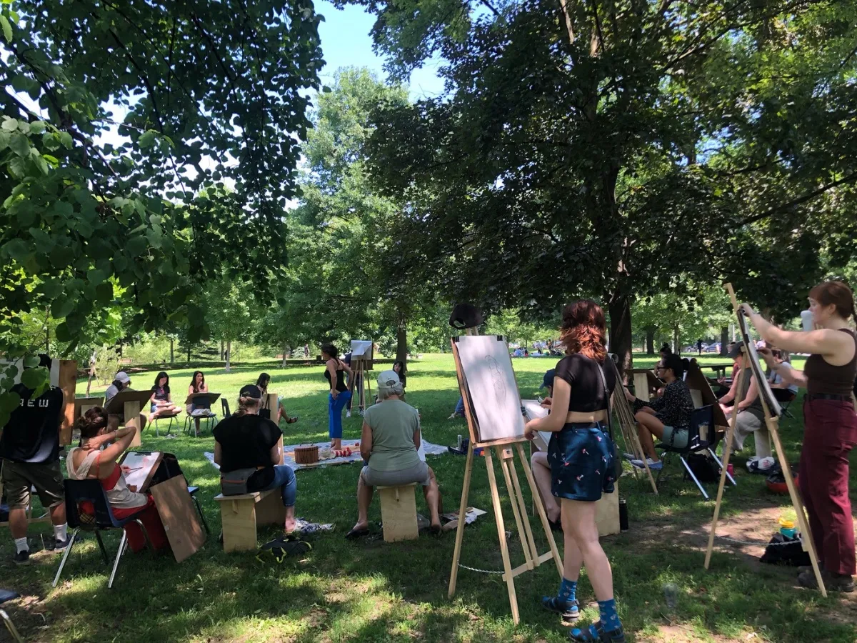 A wide view of a session: artists at easels and on benches in a sunny park.