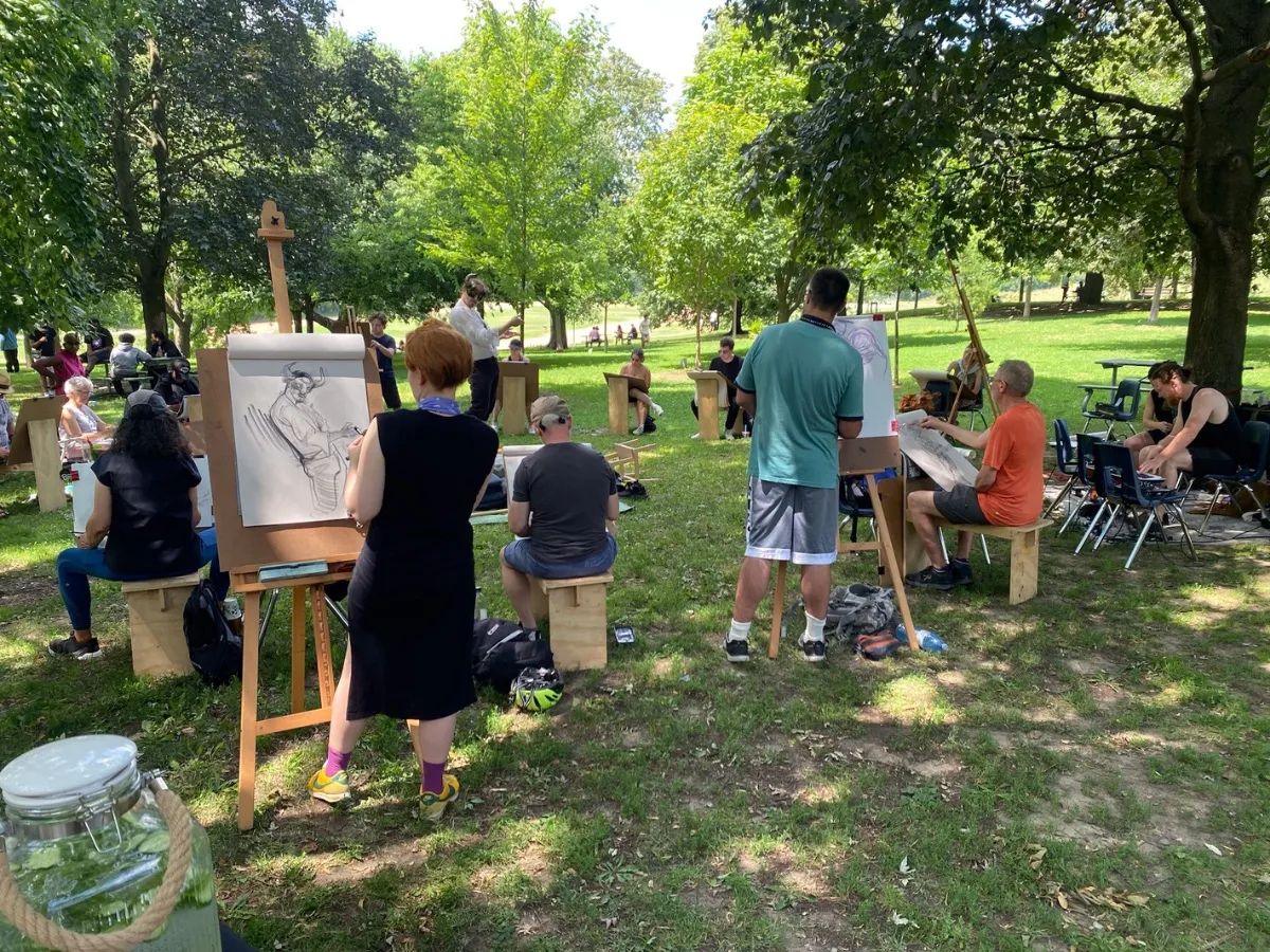 Artists at easels and benches work in a circle on the grass.