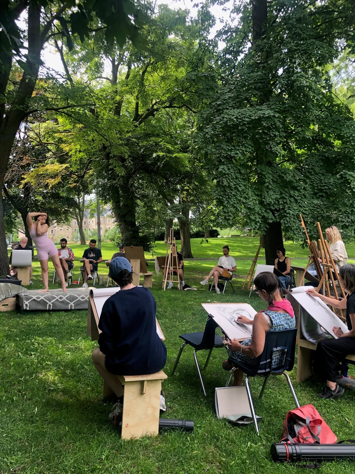 A model holds a dance pose on a platform while seated artists draw around her.
