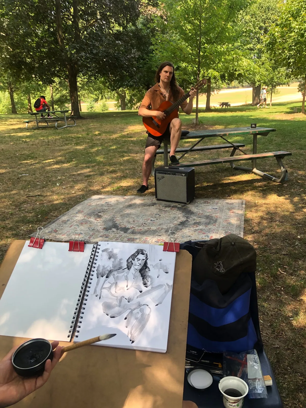 An ink drawing of a guitarist in a sketchbook, with the guitarist playing on a rug in the background.