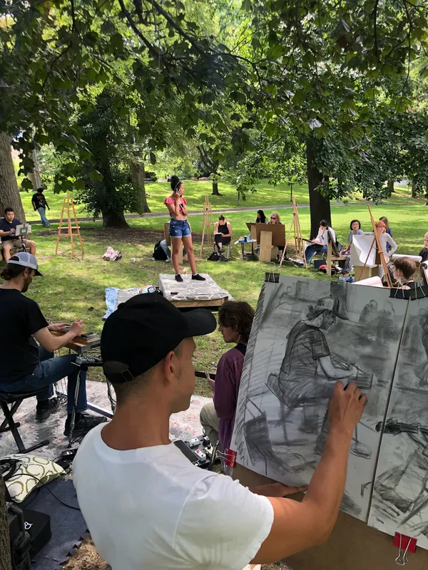 An artist draws the scene in charcoal while a model stands on a platform and a musician plays.