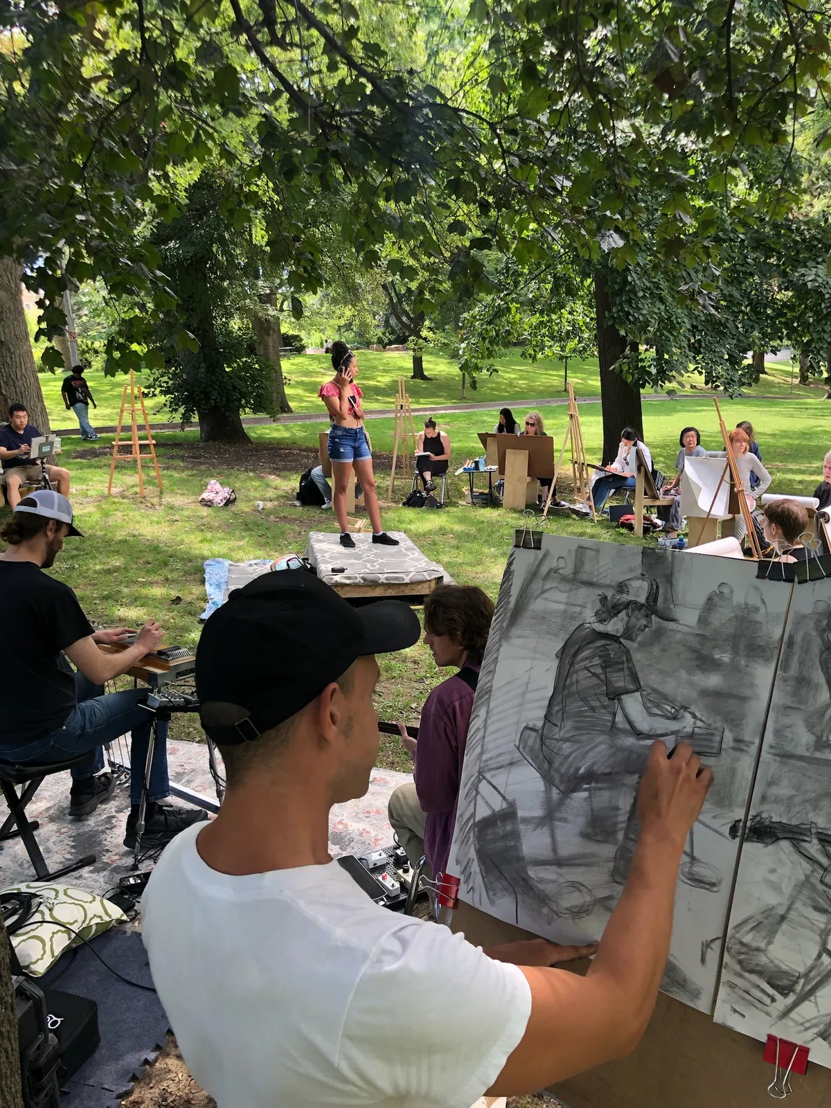An artist draws the scene in charcoal while a model stands on a platform and a musician plays.