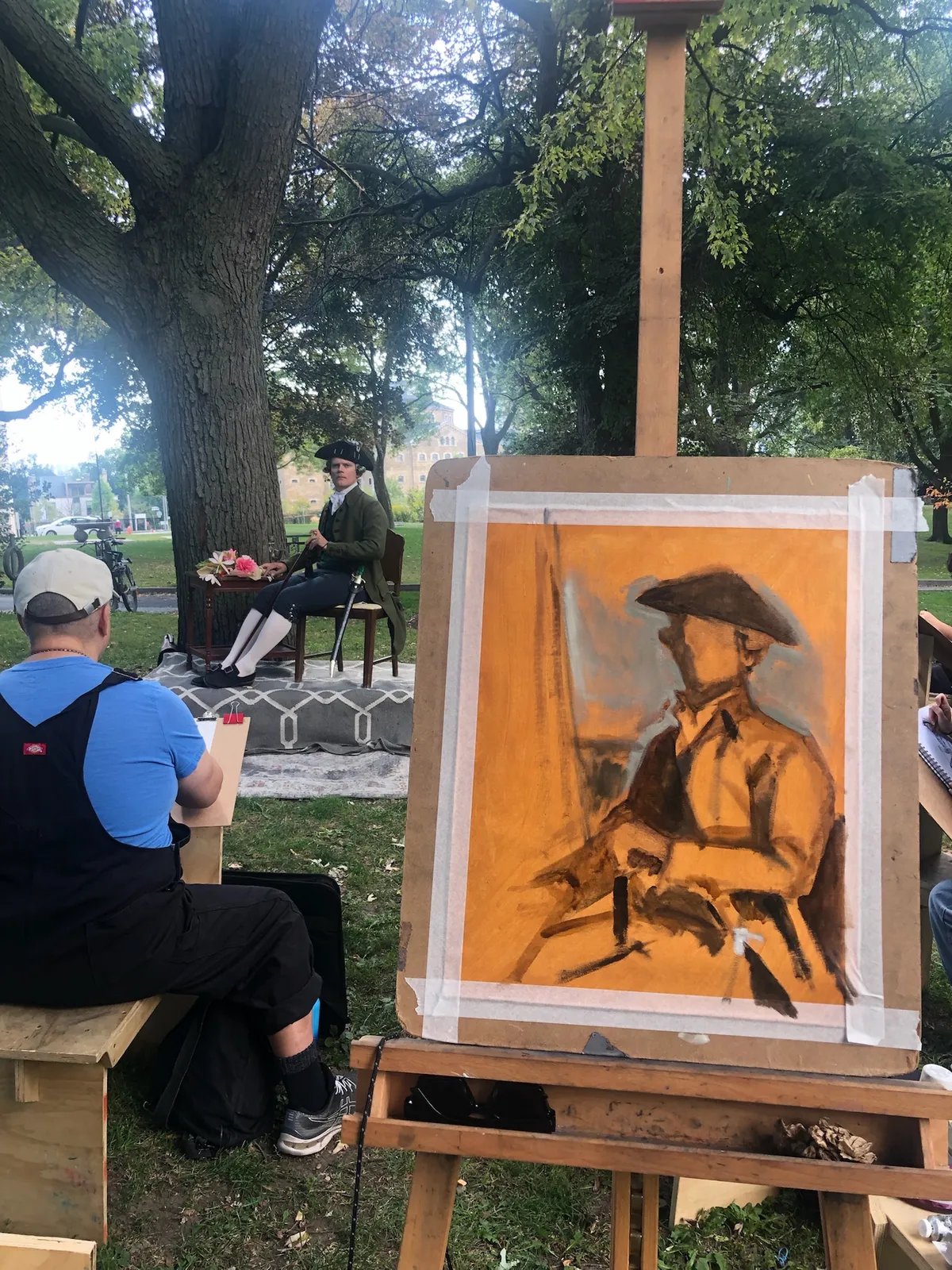 A sepia chalk drawing of the costumed model on an easel, with the model posing in the background.