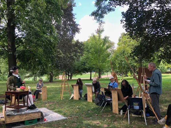 The costumed model poses under a tree while a semicircle of artists draws.