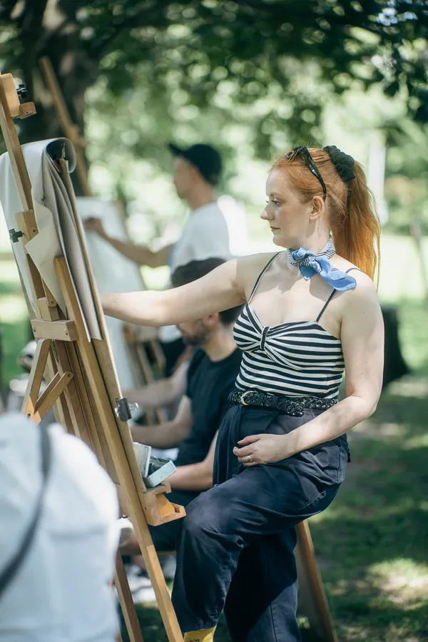 A woman in a striped top works at an easel in the park.