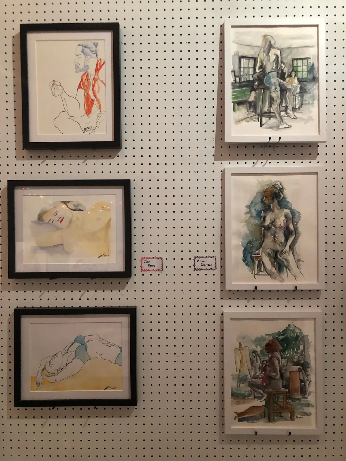Six framed figure drawings and watercolours hung on a white pegboard wall.