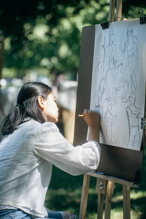 A young woman sketches a page of quick gesture figures on an easel.