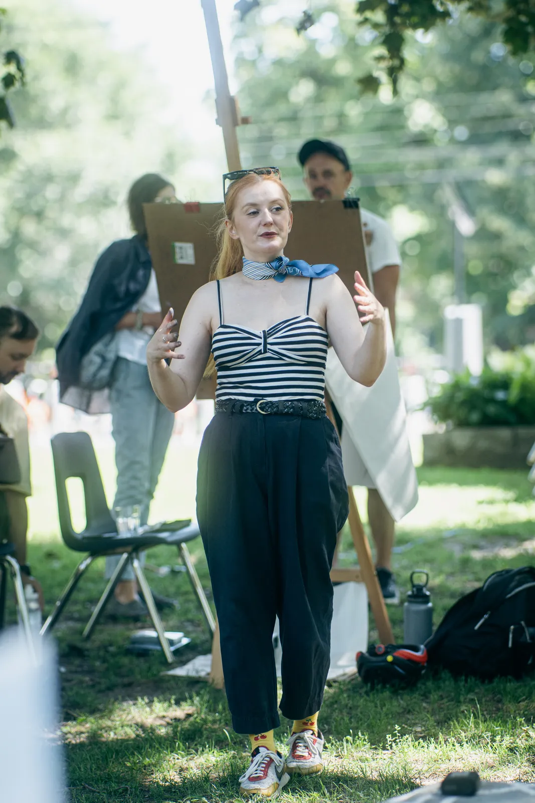 The model, in a striped top and scarf, gestures as she poses among the easels.