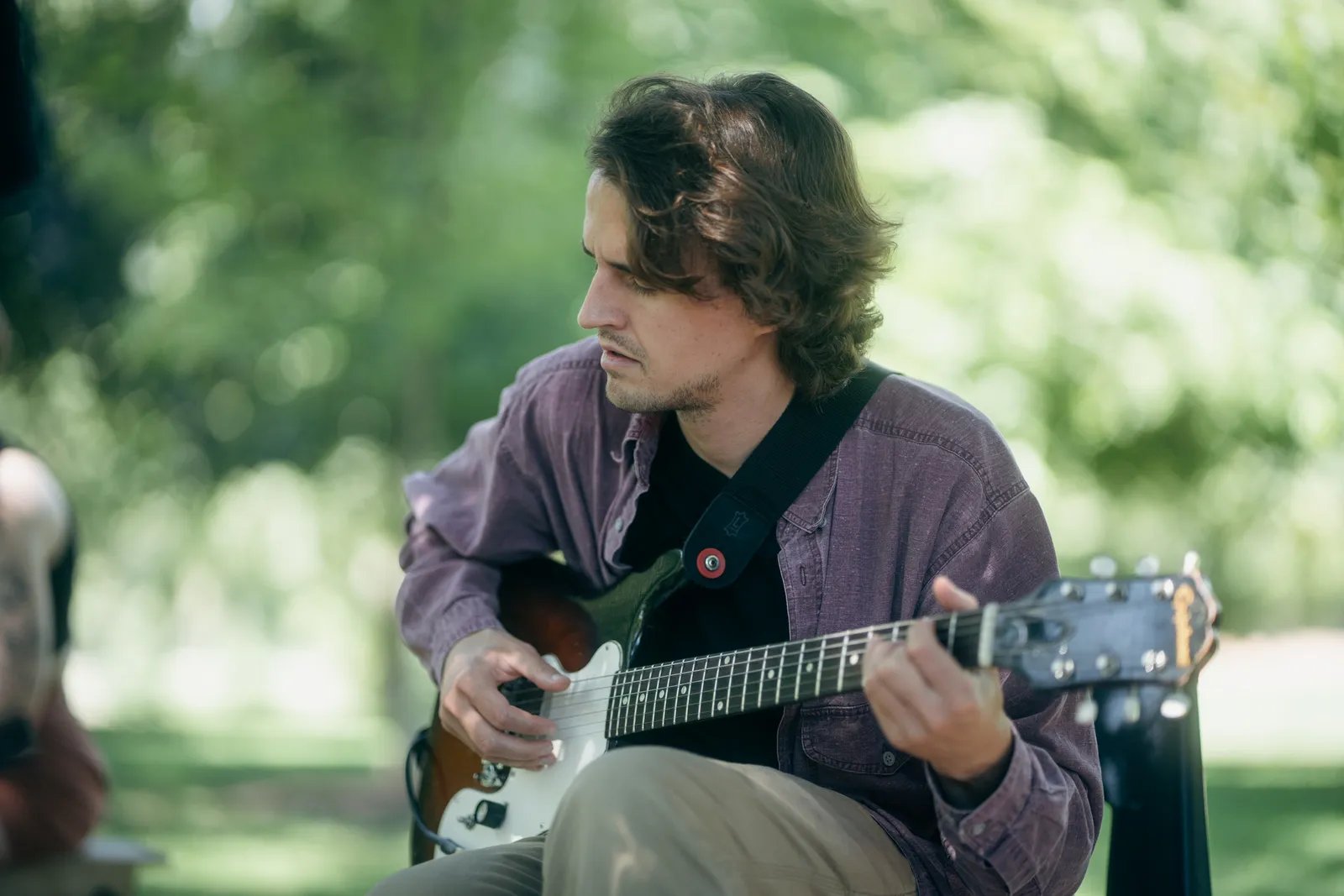 A guitarist plays an electric guitar in the shade.